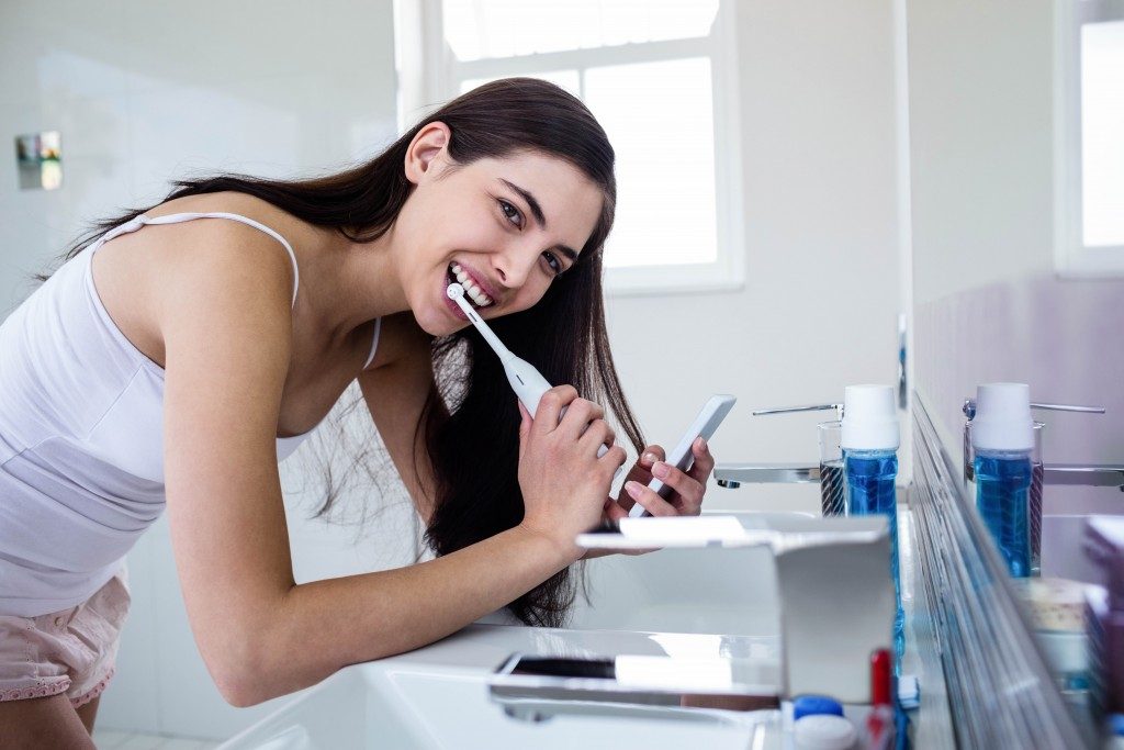 Woman brushing her teeth while using her smartphone