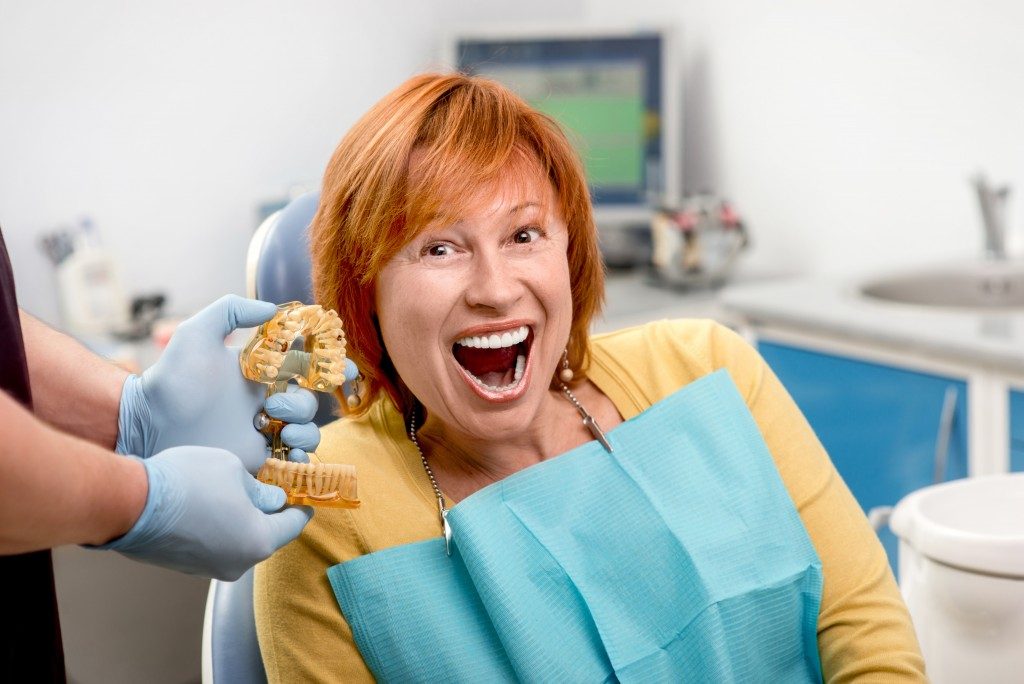 Smiling senior woman with new dental implants sitting in the dental office