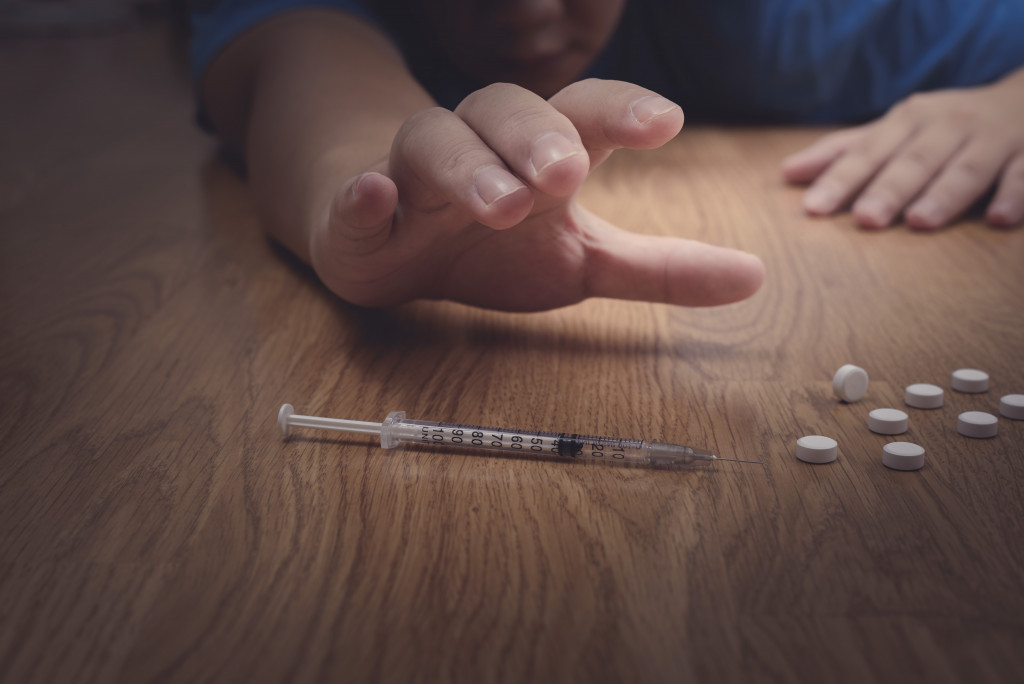 man reaching out for a syringe and drugs while crouching