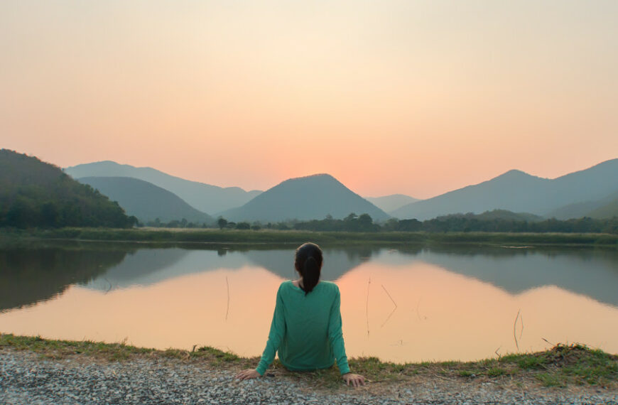 woman meditating in front of a lake with mountains in the distance