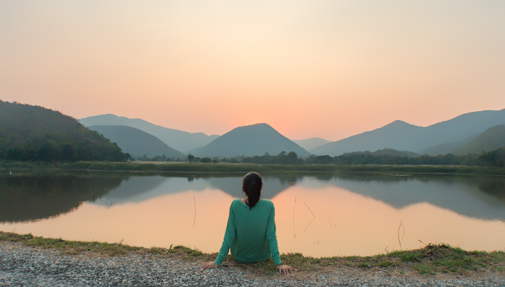 woman meditating in front of a lake with mountains in the distance