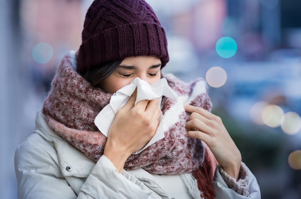 woman blowing her nose with a tissue outdoor in winter
