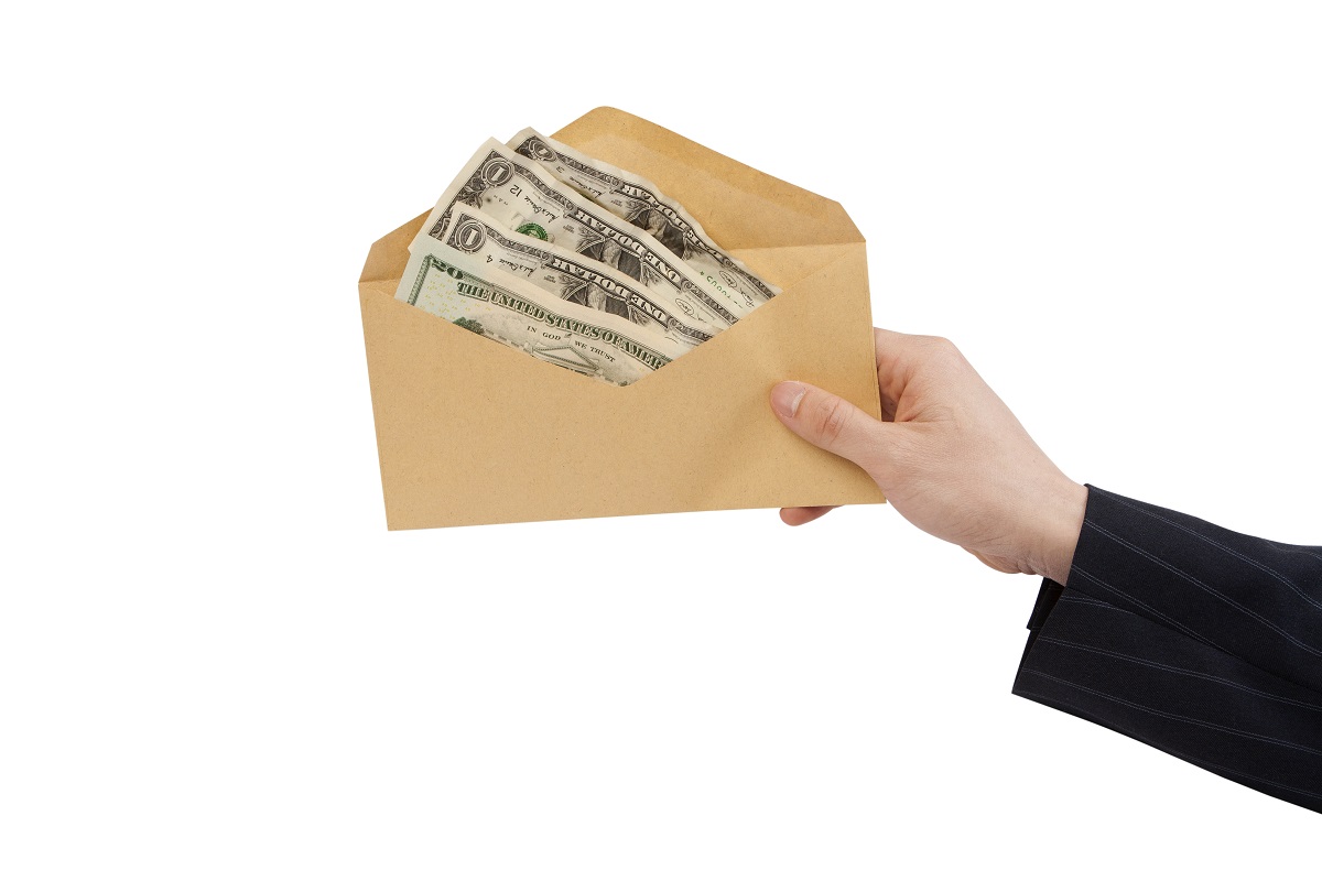 A person's hand holding out an envelop filled with money.